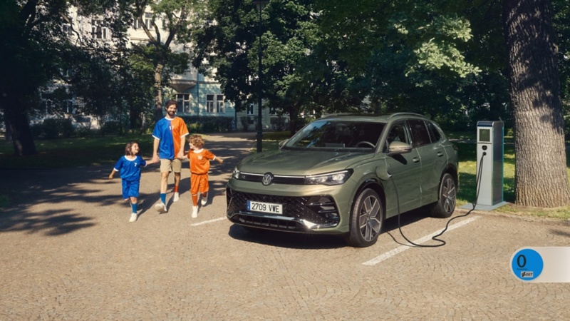 Un padre con sus hijos al lado de un Volkswagen Tiguan híbrido enchufable de color verde conectado a carga estacionado en la calle