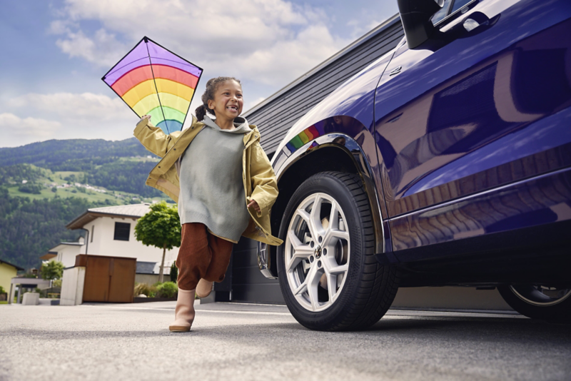 Ett barn springer med en färgglad drake förbi en blå Volkswagen familjebil