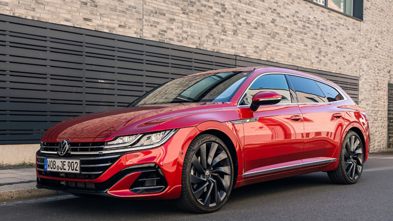 A red Volkswagen Arteon Shooting Brake parked on a city street next to a brick building.