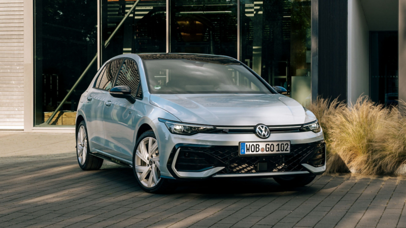 A silver Volkswagen Golf eTSI hatchback parked in front of a modern glass building.
