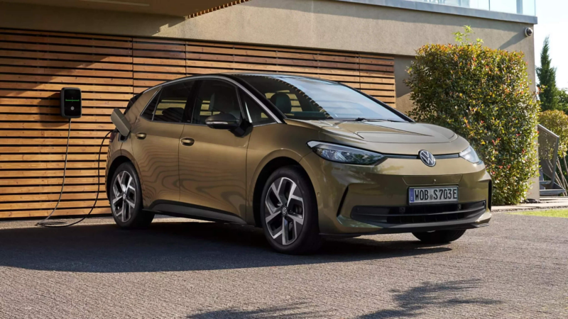 An ID.3 parked in a driveway while charging from a wallbox mounted on a slatted wooden wall.