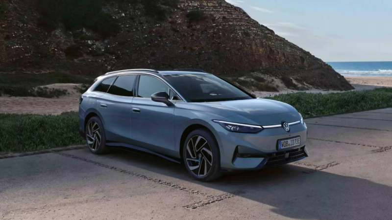 A Volkswagen ID.7 Tourer parked on a paved coastal overlook with a rocky cliff and the ocean in the background.