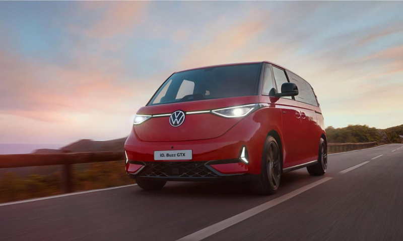 Front view of a red Volkswagen ID. Buzz GTX driving on a coastal road during sunset.