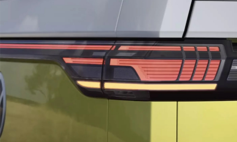 A close-up of the modern LED taillight assembly on a two-tone Volkswagen vehicle, featuring an illuminated orange and red light strip against a silver and green body.