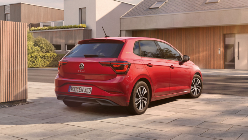 Rear view of a red Volkswagen Polo eTSI parked on a stone driveway in front of modern houses.