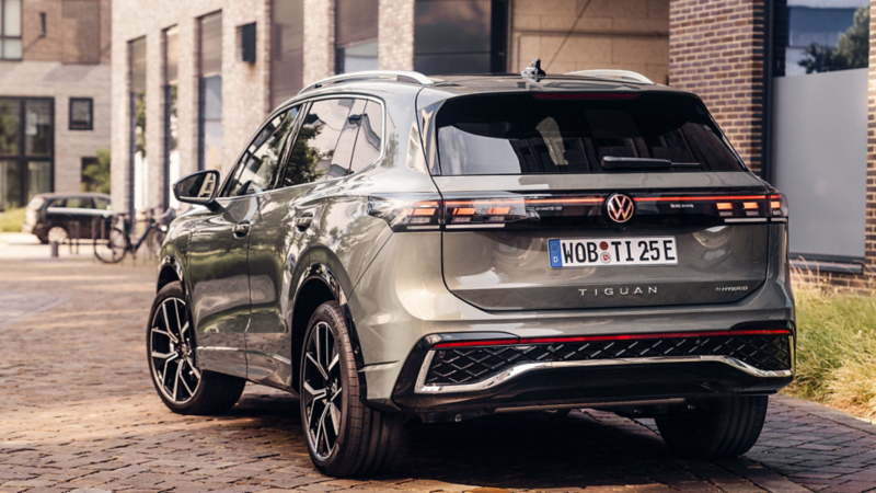 Rear view of a metallic grey Volkswagen Tiguan SUV parked on a cobblestone street in front of a modern brick building.