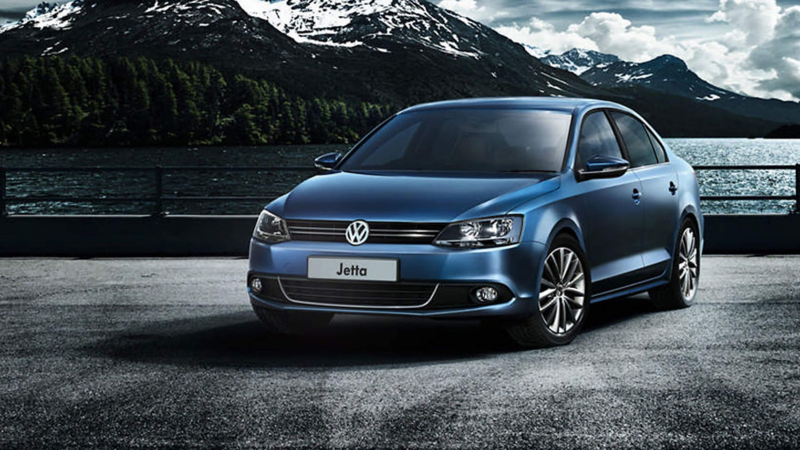 A parked Blue Jetta with the sea behind it