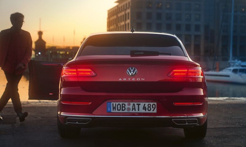 A view of the tail lights of a red Arteon Shooting Brake, with a man entering the passenger side.