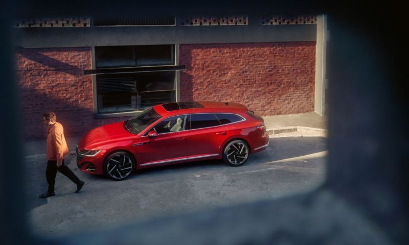 A side view of a red Arteon Shooting Brake on the street, from a window.