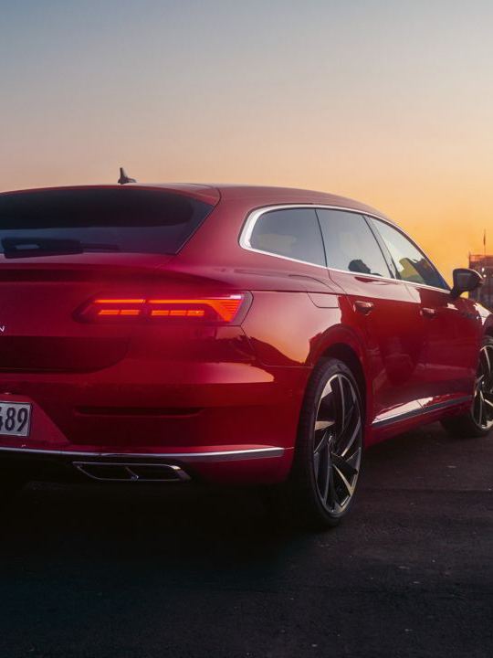 A tail light view of a red Arteon Shooting Brake parked at a dock, with a man and dog walking alongside it.