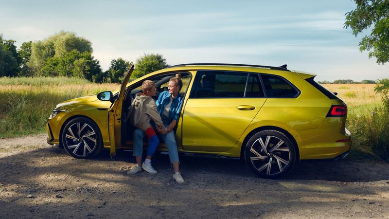A woman and child sat in a parked yellow Golf Estate 8 in a field.