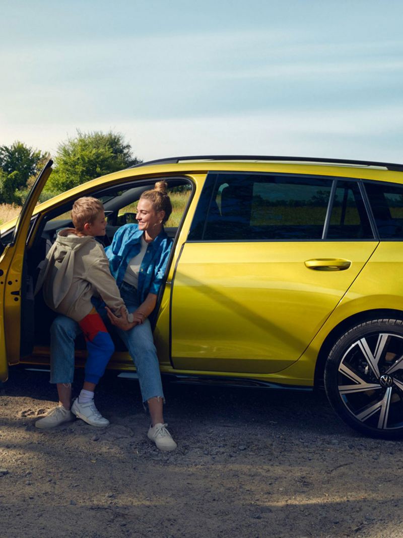 A woman and son sat in a parked yellow Golf Estate 8 in a field.