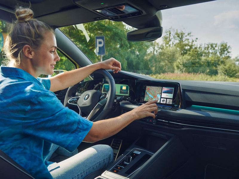 A woman sat in the driver seat of a Golf Estate and touching the infotainment screen.