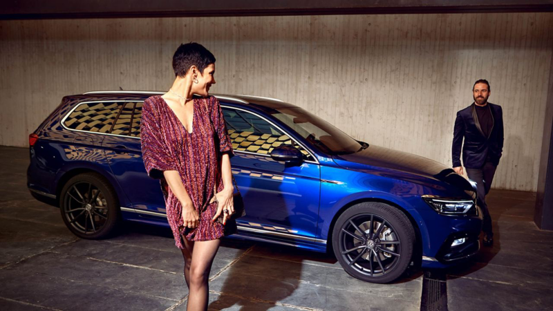 A man and woman walking by a parked VW Passat Estate