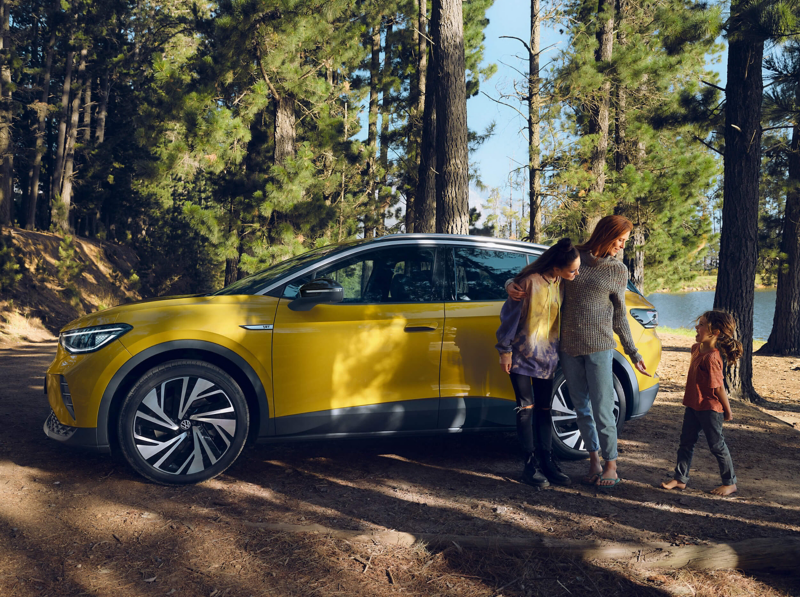 A family stood next to their yellow ID.4 in a woodland setting.