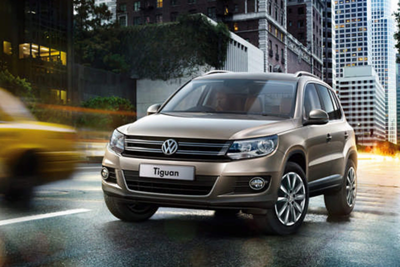 A bronze Volkswagen Tiguan, driving through a city in the evening.