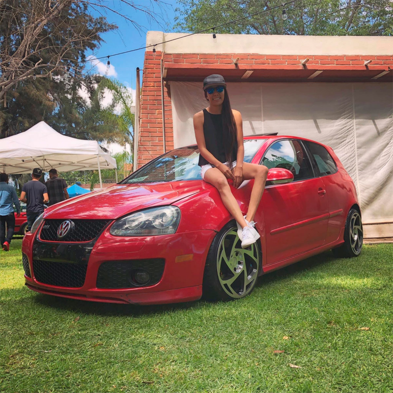 Fátima Castañón sentada sobre su auto hatchback Volkswagen Golf GTI MK5.