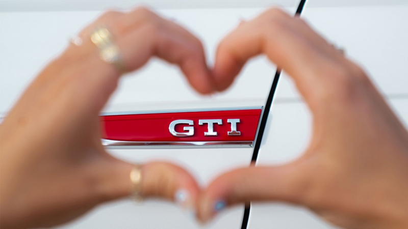 A person making a heart shape with their hands over the GTI emblem