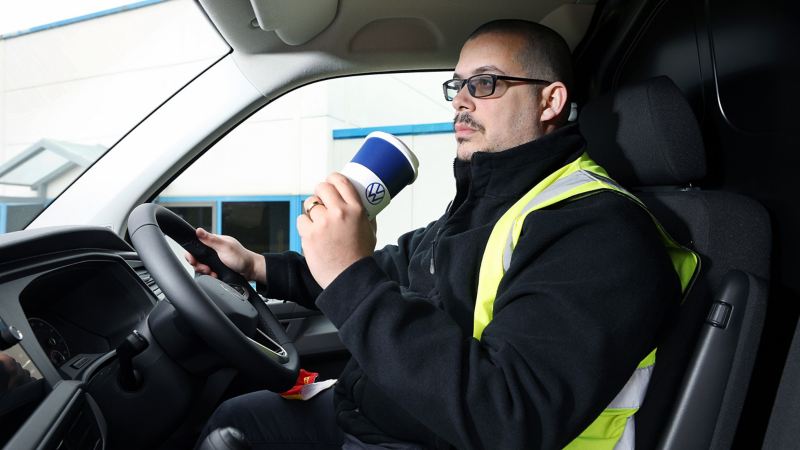 A driver inside a VW Van cockpit drinking from a coffee cup.