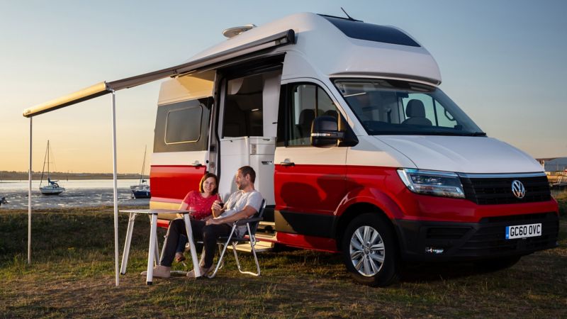 A photo showing a couple sitting outside, next to a Grand California. 