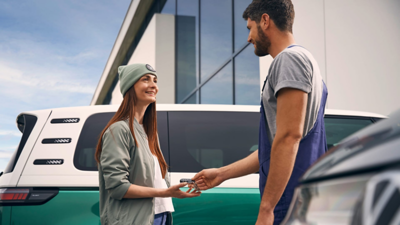 Una mujer recibiendo unas llaves delante de un VW ID. Buzz.