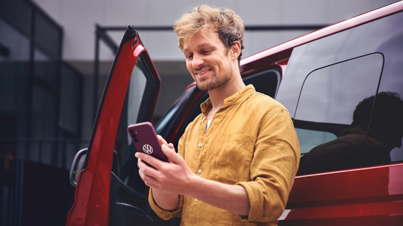 Un hombre usando un móvil con una furgo VW de color granate de fondo.