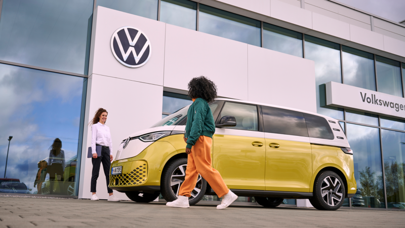 Una mujer del servicio técnico de VW hablando con una mujer, al lado del VW ID. Buzz.