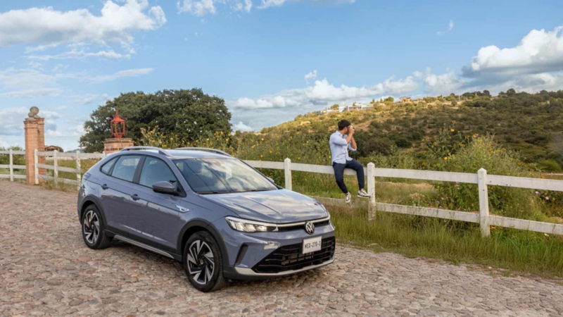 Hombre toma foto al paisaje mientras un Nivus 2026 color gris está sobre camino empedrado. 