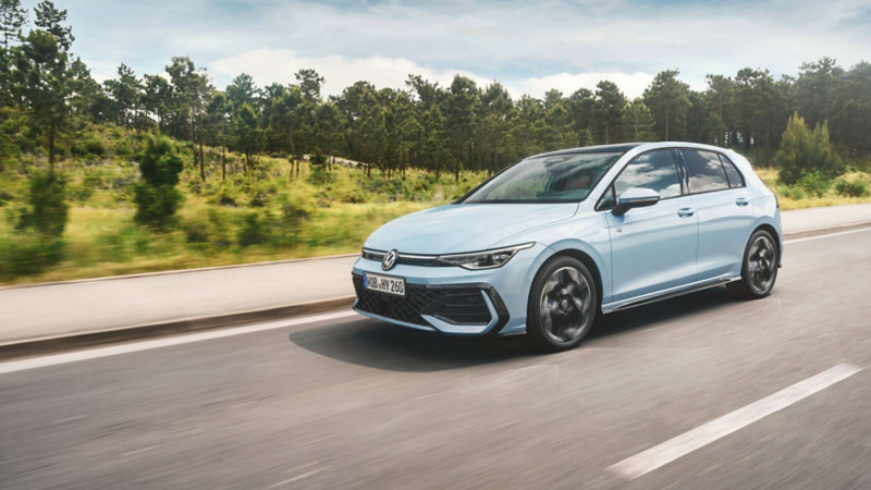 Hatchback Volkswagen Golf azul claro avanza por una carretera junto a una zona arbolada.