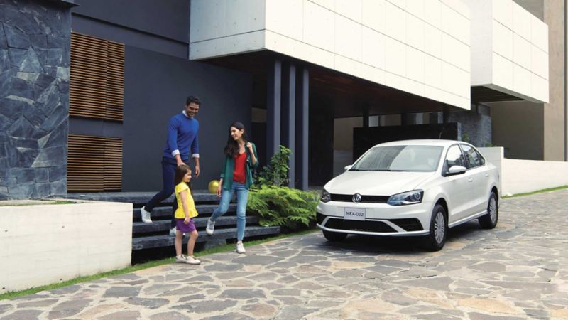 Vento 2022 Startline en color blanco estacionado a fuera de una casa. Familia se dirije al auto sedán. 
