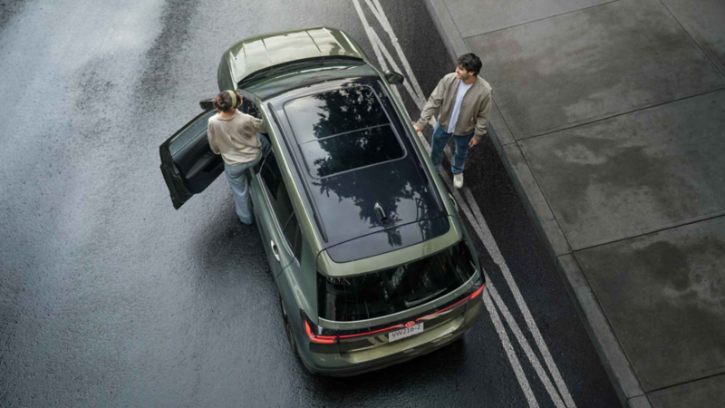 Volkswagen Taigun verde visto desde arriba; una mujer abre la puerta y un hombre espera afuera.