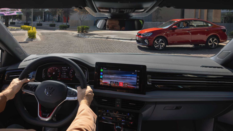 Interior de un auto Volkswagen. Conductor toma volante mientras conduce, dentro de una ciudad. 