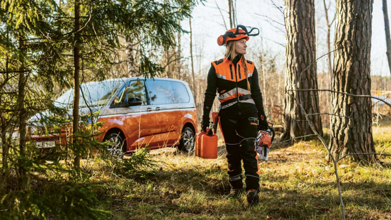 Arboristen Victoria Carstens på väg ut i skogen på jobb, i bakgrunden en VW Multivan e-Hybrid minibuss