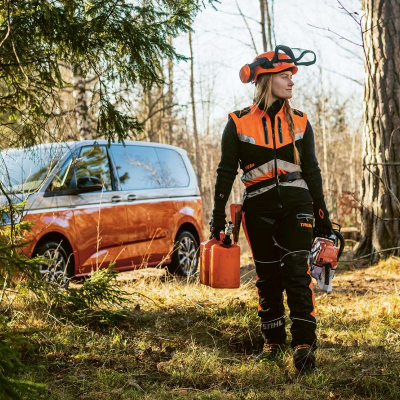 Arboristen Victoria Carstens på väg ut i skogen på jobb, i bakgrunden en VW Multivan e-Hybrid minibuss