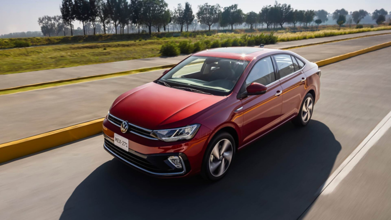 Volkswagen Virtus de color rojo transita sobre avenida con un prado al fondo.