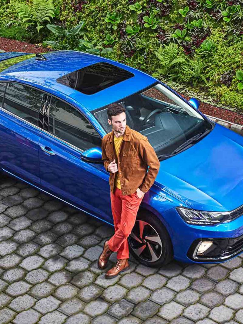 Volkswagen Virtus 2024 en color azul, con joven conductor recargado sobre sedán. 