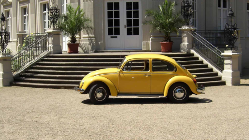 Volkswagen Sedán. Vista lateral de auto clásico de color amarillo estacionado frente a edificio.