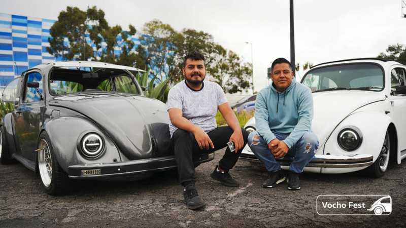 Dos propietarios de Vocho posan mientras están sentados en la defensa de sus autos. 
