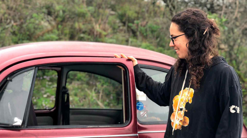 Vocho de color rojo, con mujer abriendo la puerta de piloto. 
