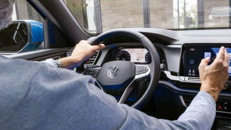 Conductor toma volante multifunciones de Volkswagen y toca la pantalla para elegir aplicación. 