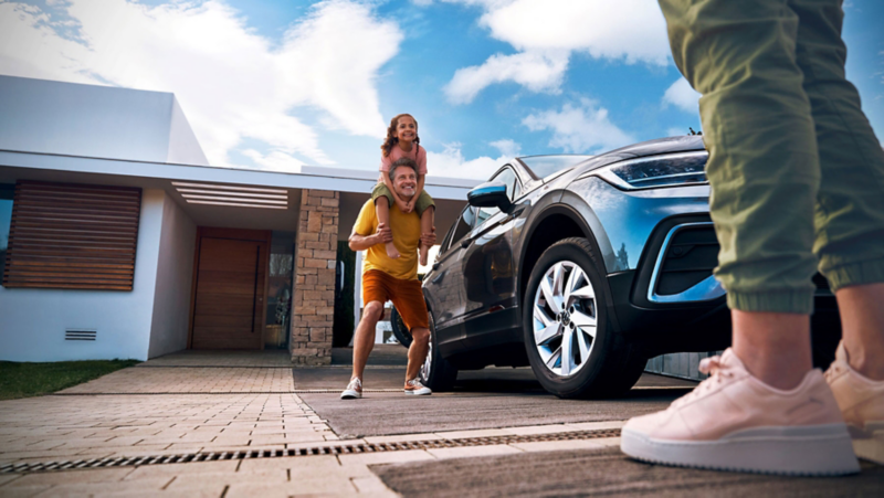 Family standing outside a house beside a VW Tiguan Allspace in Platinum Grey Metallic