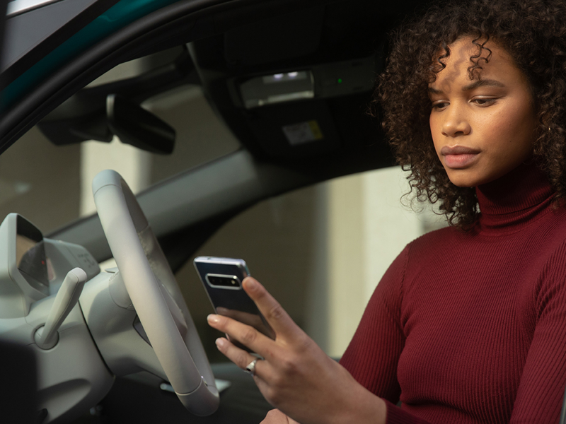 Woman looking at her phone will sitting in a VW ID. car
