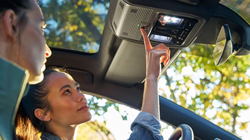 Two women in a car, driver presses button for Volkswagen Emergency Service