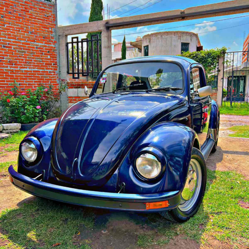 Volkswagen Sedán. Vista frontal de auto clásico de color azul oscuro estacionado sobre pasto.