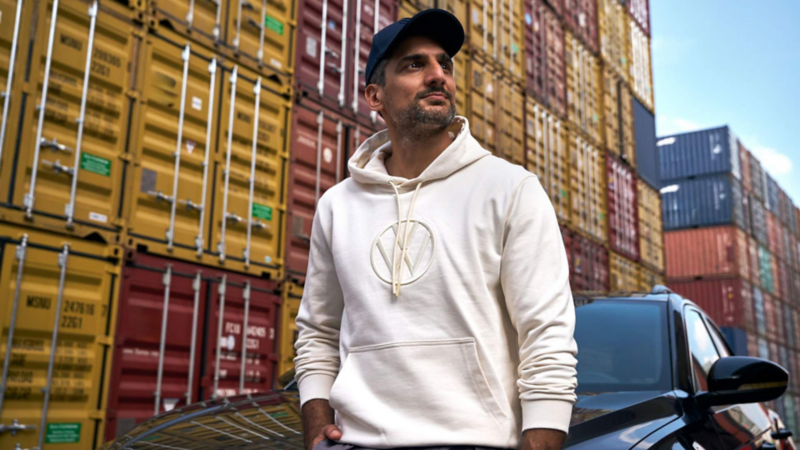 Hombre con gorra y sudadera Volkswagen Essentials junto a un automóvil.