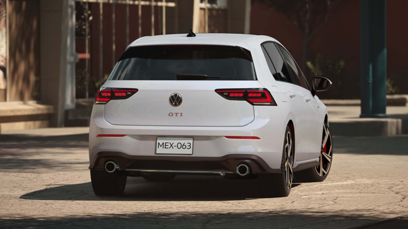 GTI 2025 de color blanco pasa una curva dentro de una carretera rodeada de árboles.