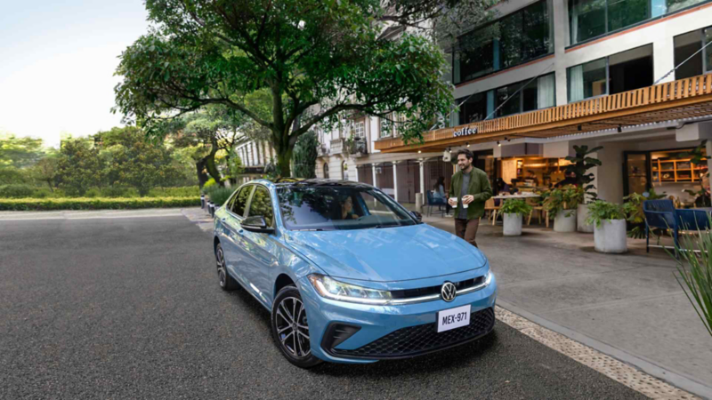 Volkswagen Jetta de color azul. Vista frontal en tres cuartos junto a una calle arbolada y locales comerciales.Modificado con inteligencia artificial