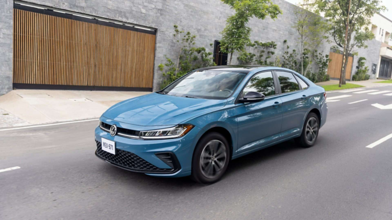 Volkswagen Jetta de color azul circulando por avenida urbana. Sedán deportivo con parrilla renovada y rines de aluminio.