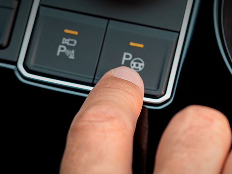 Que son sensores de reversa y Park Assist de Volkswagen - Dedo oprime botón de park assist en SUV.