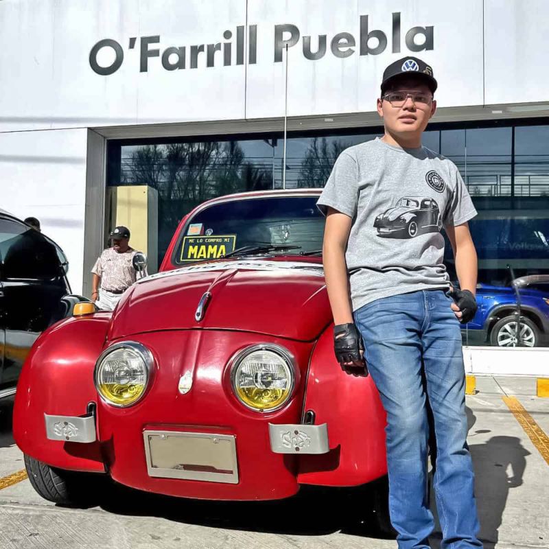 Joven posa frente a Vocho de colección de color rojo. 